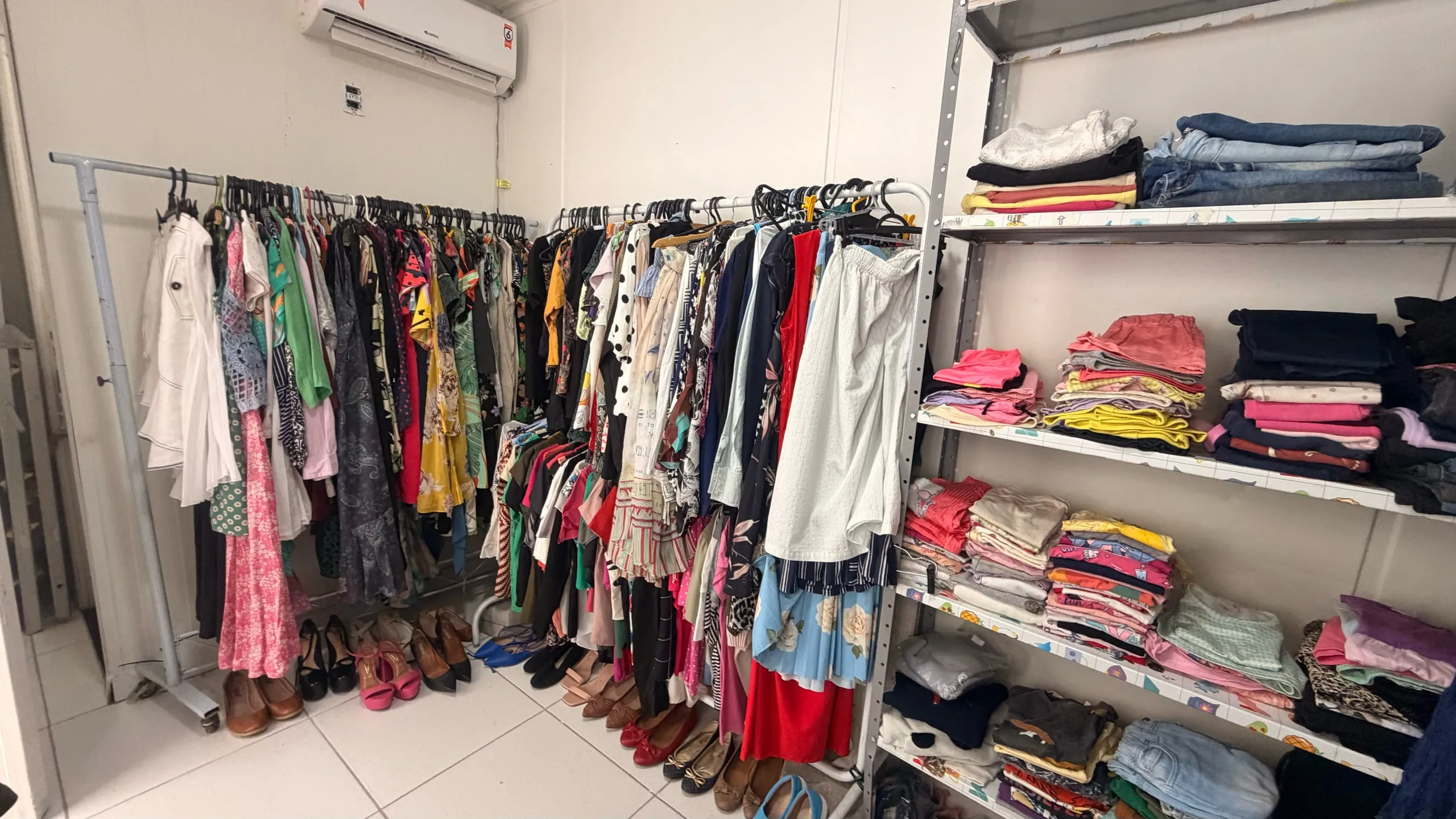Araras com roupas e prateleiras de peças dobradas no brechó.