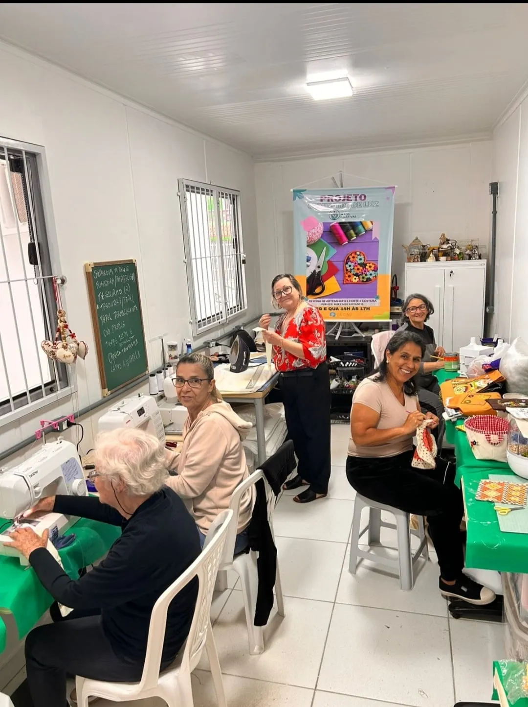 Integrantes do Mãos Criativas costurando e bordando em volta de uma mesa, na casa.