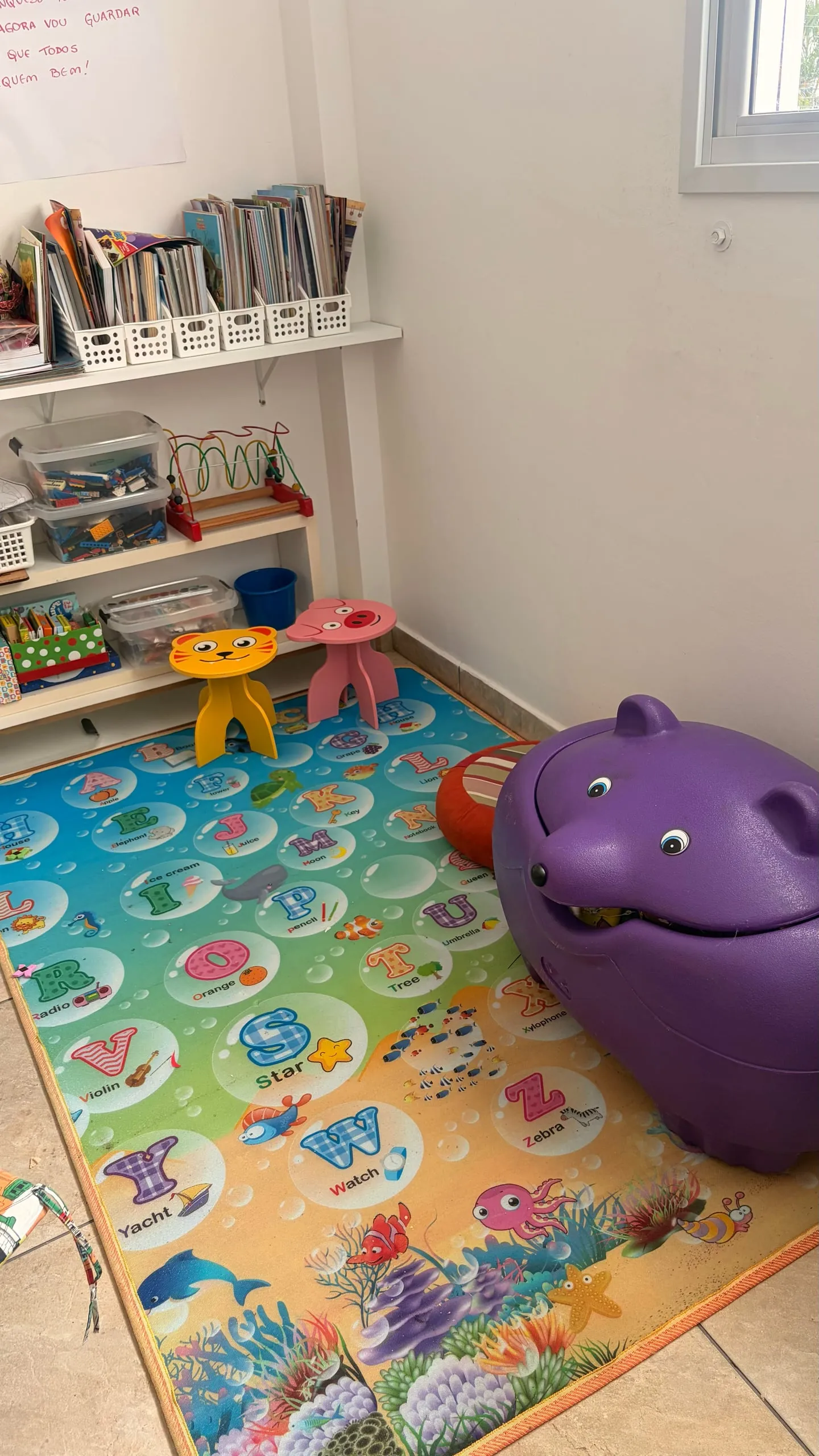 Um canto da sala das crianças, com tapete colorido, livros na estante e um bichinho de pelúcia.