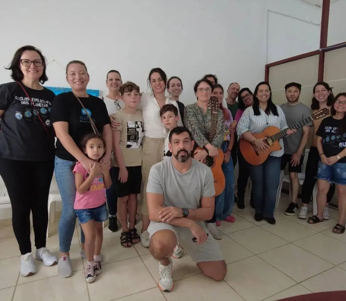 Famílias e crianças reunidas no salão do CECAL, um dos adultos com um violão no colo.