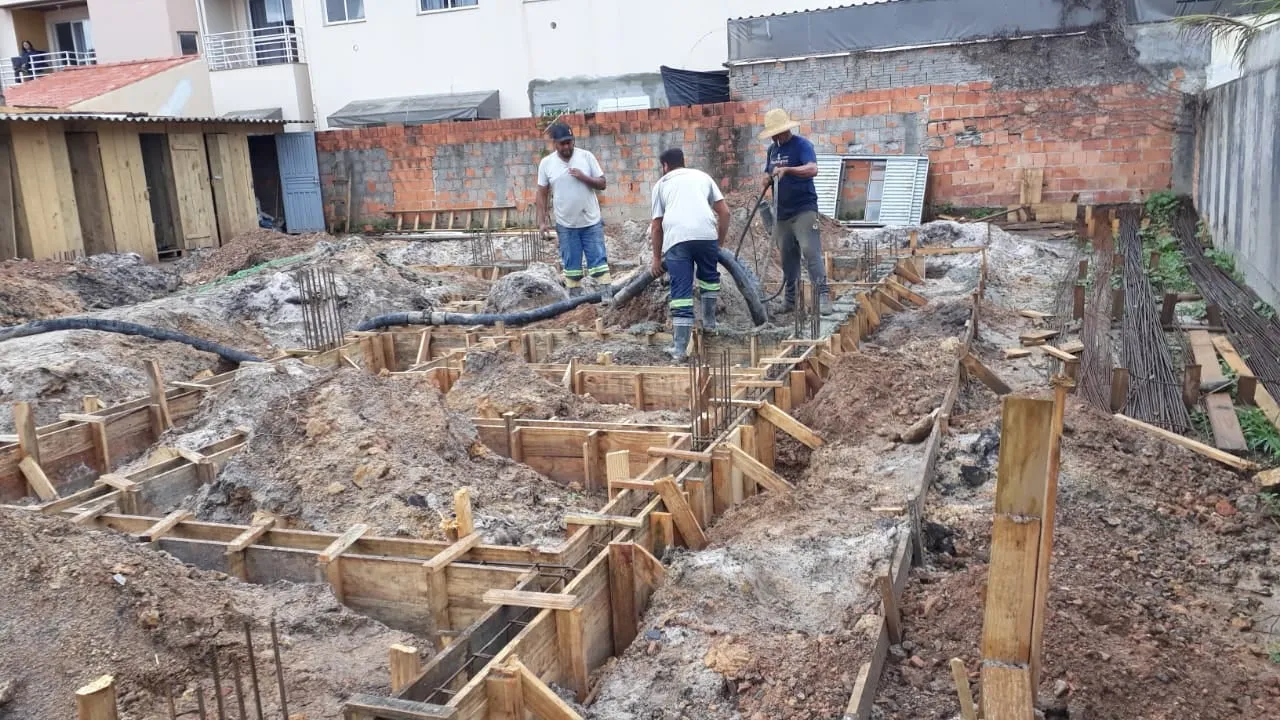 A fundação da sede em obra: formas de madeira abertas no terreno e três operários trabalhando.