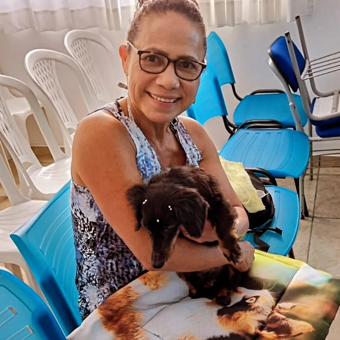 Uma senhora sentada nas cadeiras do salão, com o cachorro no colo.